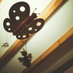 Harika bir görsel! Bu fotoğraf için hem Google'ın seveceği hem de ekran okuyucu kullanan birinin zihninde canlanacak, doğal ve SEO uyumlu seçenekler şunlar:

**Seçenek 1 (En Doğal ve Tanımlayıcı):**
> "Huzurlu bir bebek odasında, tavandaki ahşap kirişlerden sarkan masalsı ve zarif kelebekli dönence."

**Seçenek 2 (Dekorasyon Odaklı):**
> "Sıcak ve samimi bir kreş odası dekorasyonu için ahşap kirişlere asılmış, uçuşan kelebek figürlü mobil süs."

**Seçenek 3 (Kısa ve Öz):**
> "Bebek odası tavanındaki ahşap detaylarla uyumlu, hayal gücünü besleyen kelebekli dekoratif dönence."

---

**Neden bunlar işe yarar?**
*   **Robotik değil:** "Kelebek dönence bebek odası ahşap" gibi kelimeleri arka arkaya dizmek yerine, bir sahneyi betimliyor.
*   **SEO Dostu:** "Bebek odası", "kelebekli dönence", "ahşap kiriş" gibi anahtar kelimeleri doğal bir akış içinde barındırıyor.
*   **Erişilebilirlik:** Görme engelli bir kullanıcıya fotoğrafın sadece ne olduğunu değil, nasıl bir "his" verdiğini (huzurlu, masalsı, sıcak) anlatıyor.